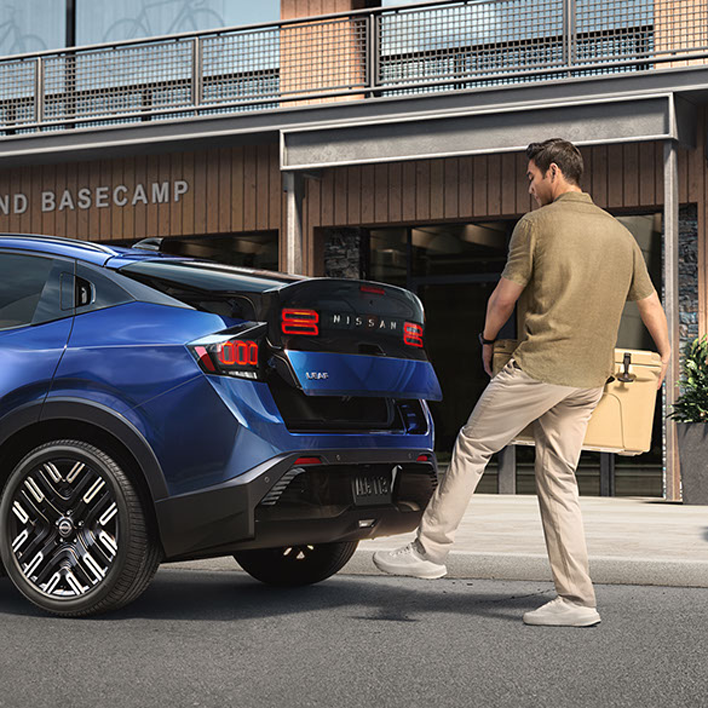 Man with cooler activating hands-free liftgate on a blue Nissan with his foot.